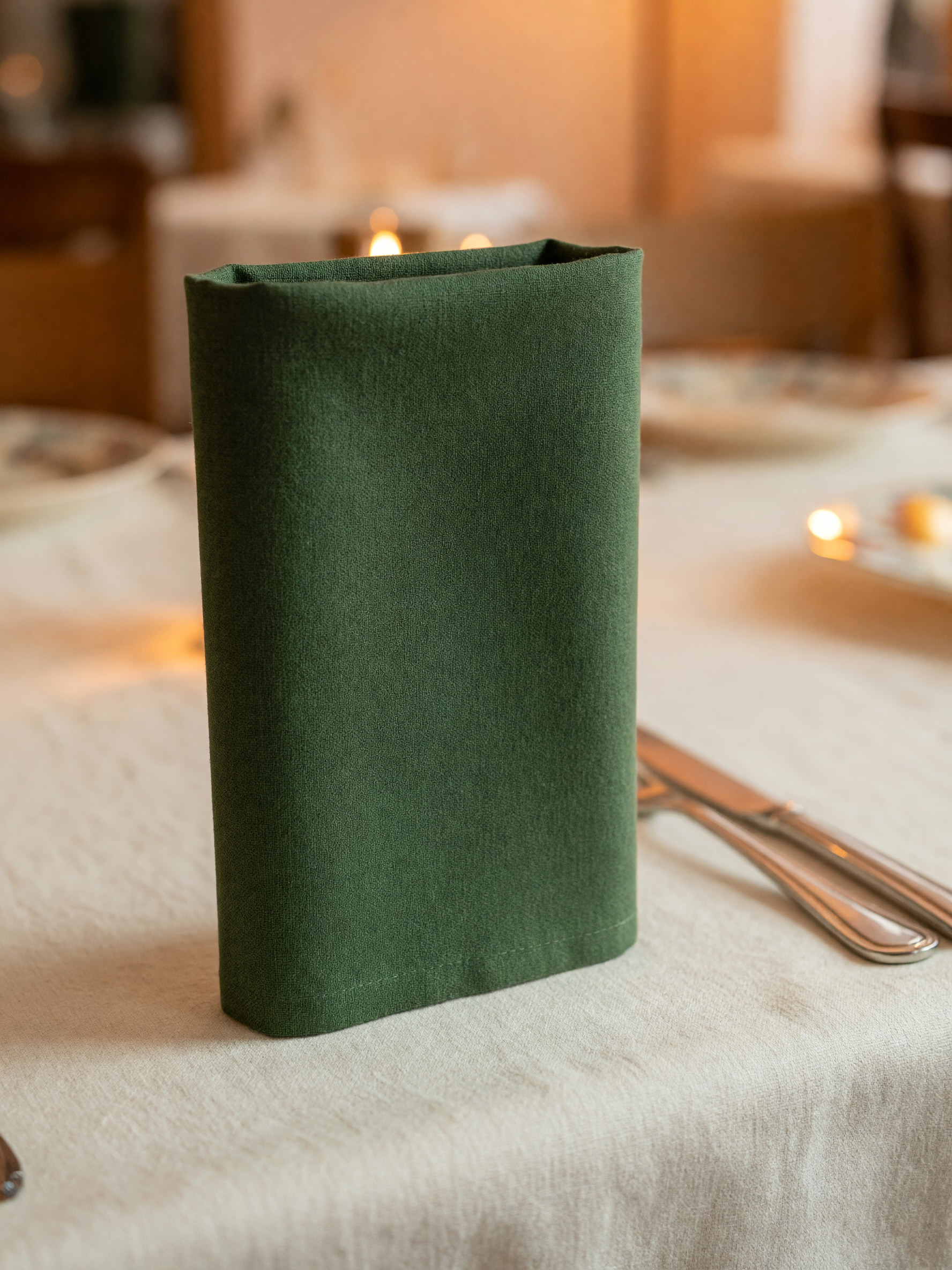 Dunkelgrüne Stoffserviette und Besteck auf weißem Leinentischtuch im warm beleuchteten Gastraum