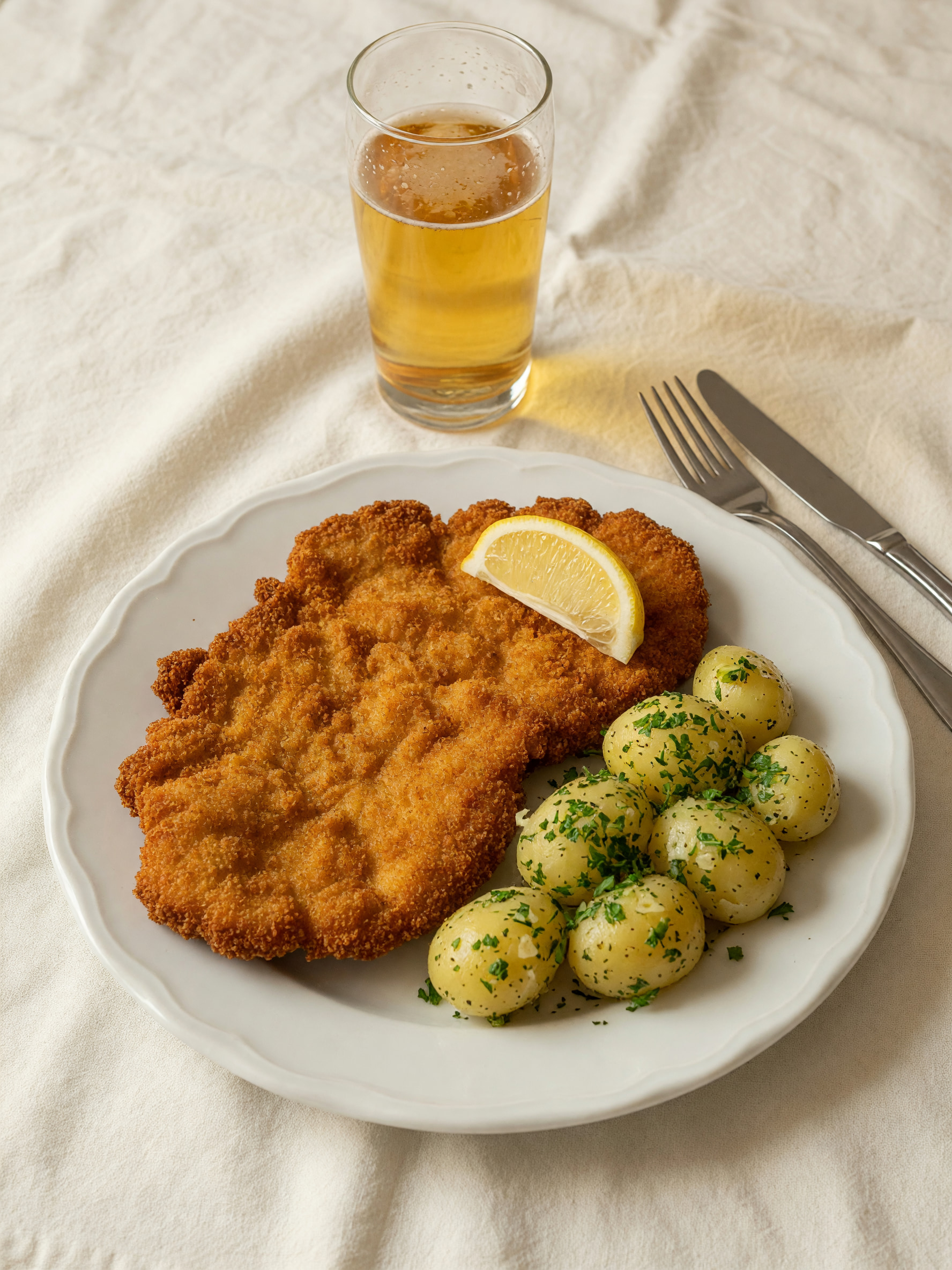 Goldbraun paniertes Schnitzel mit Zitronenschnitz und Erdäpfeln auf weißem Leinentisch